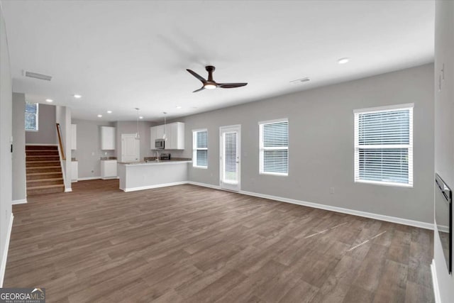 unfurnished living room featuring ceiling fan, a healthy amount of sunlight, and dark hardwood / wood-style floors