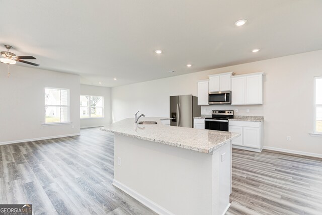 kitchen with appliances with stainless steel finishes, white cabinetry, light hardwood / wood-style floors, and an island with sink