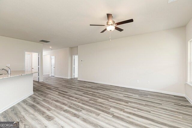 unfurnished living room with sink, ceiling fan, and light hardwood / wood-style flooring