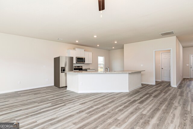 kitchen featuring light stone countertops, appliances with stainless steel finishes, light wood-type flooring, white cabinets, and a kitchen island with sink