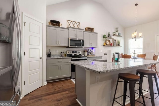 kitchen with pendant lighting, lofted ceiling, light stone countertops, appliances with stainless steel finishes, and dark hardwood / wood-style flooring