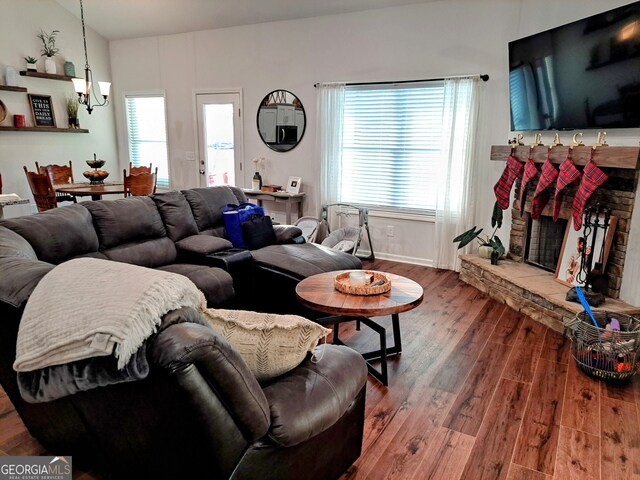 living room featuring hardwood / wood-style flooring, a stone fireplace, and a chandelier