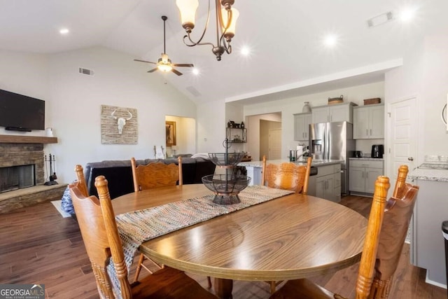 dining space featuring dark hardwood / wood-style floors, a stone fireplace, ceiling fan with notable chandelier, and high vaulted ceiling