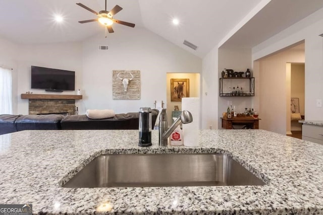 kitchen featuring lofted ceiling, sink, ceiling fan, a fireplace, and light stone counters