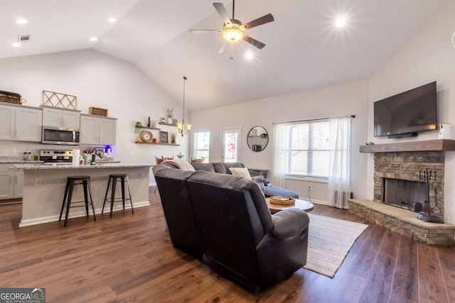 living room featuring ceiling fan with notable chandelier, dark wood-type flooring, sink, high vaulted ceiling, and a stone fireplace