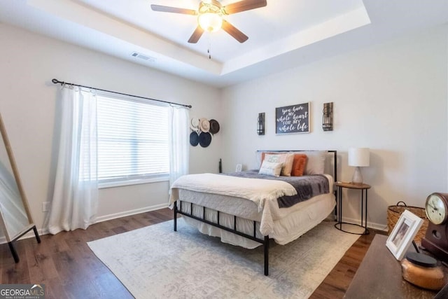 bedroom with ceiling fan, dark hardwood / wood-style flooring, and a tray ceiling