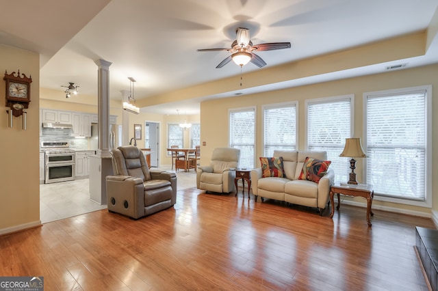 living room with decorative columns, ceiling fan with notable chandelier, and light hardwood / wood-style flooring