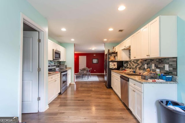 kitchen featuring sink, white cabinetry, appliances with stainless steel finishes, light hardwood / wood-style floors, and tasteful backsplash