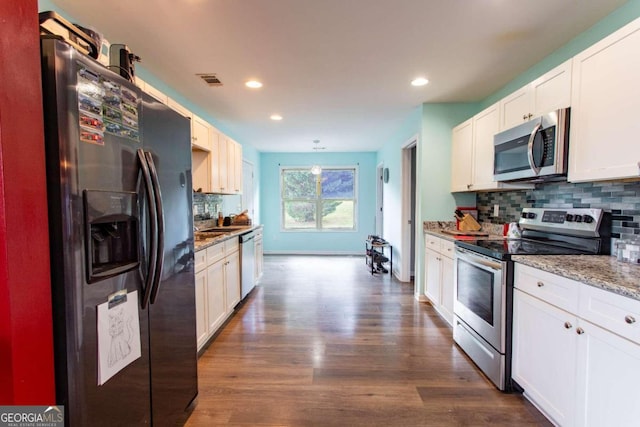 kitchen with appliances with stainless steel finishes, backsplash, white cabinetry, dark wood-type flooring, and light stone counters