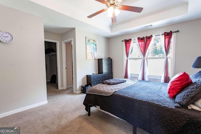 bedroom with a closet, a spacious closet, a raised ceiling, carpet floors, and ceiling fan