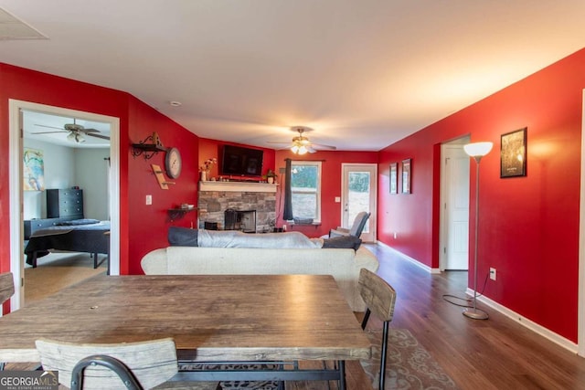 dining room featuring ceiling fan, a stone fireplace, and wood-type flooring