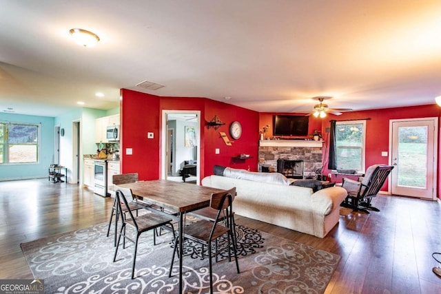 dining room featuring ceiling fan, a healthy amount of sunlight, dark hardwood / wood-style flooring, and a fireplace