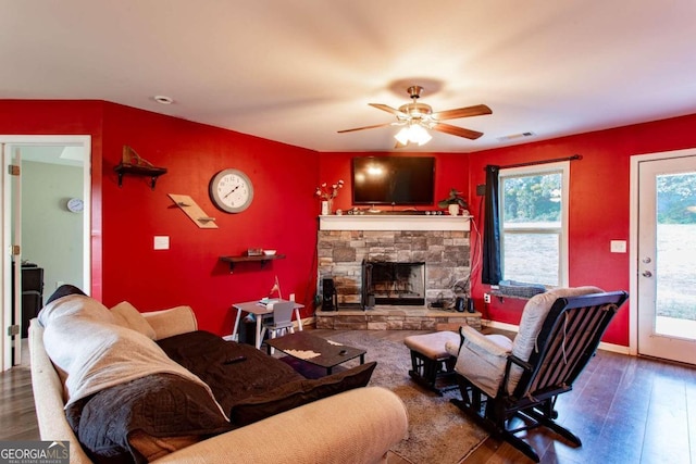 living room with a stone fireplace, wood-type flooring, and ceiling fan