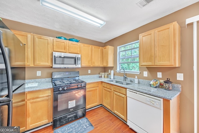 kitchen with light stone countertops, appliances with stainless steel finishes, sink, a textured ceiling, and light hardwood / wood-style floors