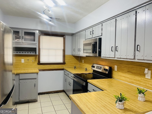 kitchen featuring a textured ceiling, light tile patterned flooring, light countertops, appliances with stainless steel finishes, and glass insert cabinets