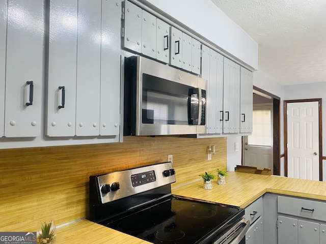 kitchen with appliances with stainless steel finishes, light countertops, a textured ceiling, and gray cabinetry