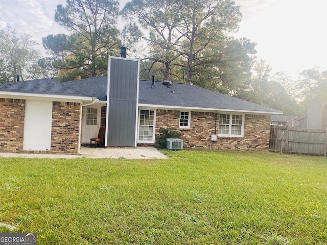 rear view of property featuring brick siding, a yard, a patio, central AC, and fence