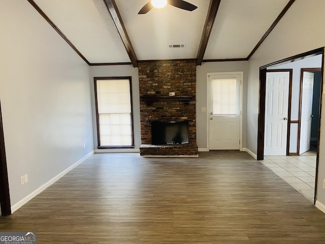 unfurnished living room with vaulted ceiling with beams, visible vents, a ceiling fan, a brick fireplace, and wood finished floors