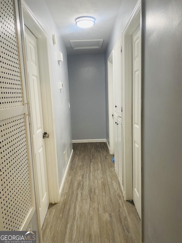 corridor with light wood-style flooring, attic access, and baseboards