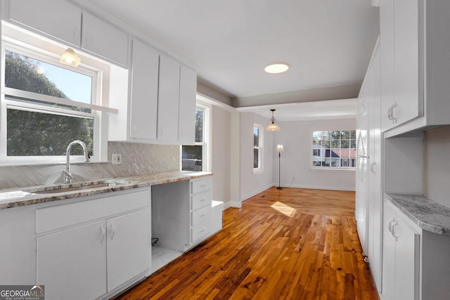 kitchen with sink, hanging light fixtures, white cabinets, light hardwood / wood-style floors, and backsplash