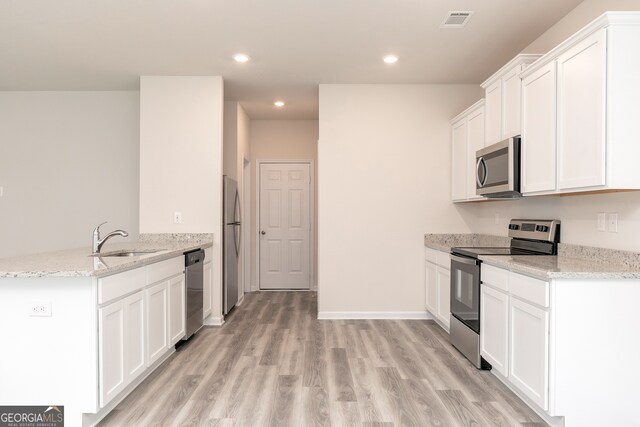 kitchen with light stone countertops, appliances with stainless steel finishes, sink, light wood-type flooring, and white cabinetry