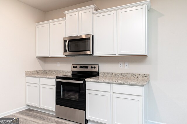 kitchen featuring light stone countertops, white cabinets, light hardwood / wood-style flooring, and stainless steel appliances