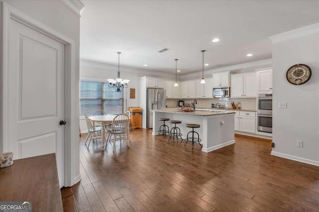 kitchen with a kitchen bar, an island with sink, white cabinetry, stainless steel appliances, and dark hardwood / wood-style floors