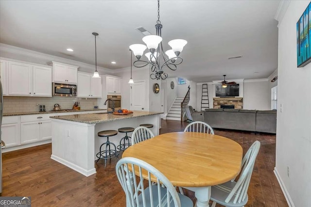 dining area featuring a stone fireplace, ornamental molding, ceiling fan with notable chandelier, and dark hardwood / wood-style flooring