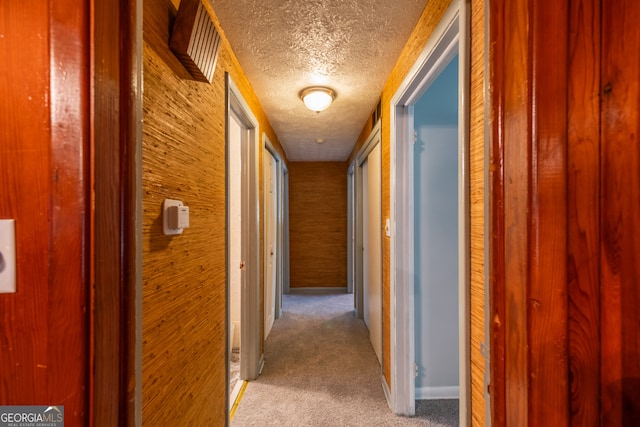 hallway featuring wooden walls, a textured ceiling, and light colored carpet