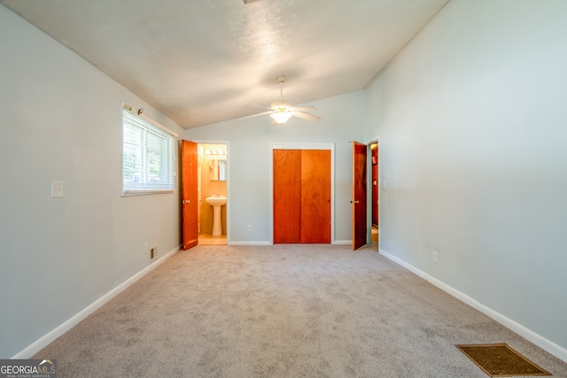 unfurnished bedroom with ensuite bathroom, vaulted ceiling, light colored carpet, and ceiling fan