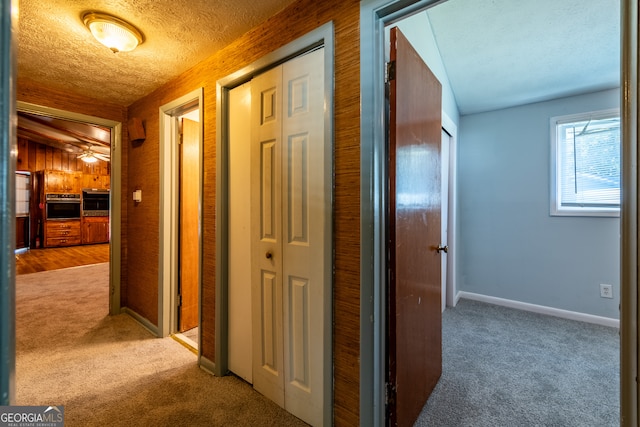 corridor featuring wood walls, a textured ceiling, and carpet