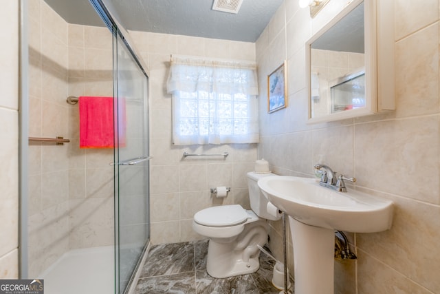 bathroom featuring a shower with door, tile walls, a textured ceiling, and toilet