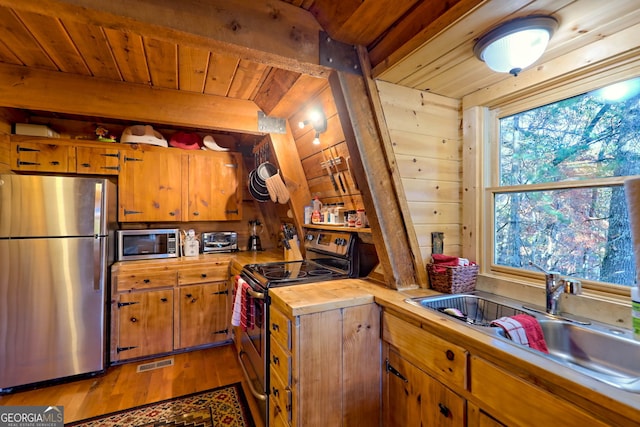 kitchen with wood ceiling, hardwood / wood-style floors, wood walls, sink, and stainless steel appliances