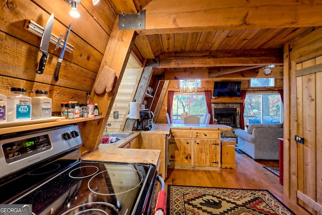 kitchen with beam ceiling, kitchen peninsula, hardwood / wood-style floors, a fireplace, and stainless steel electric range oven