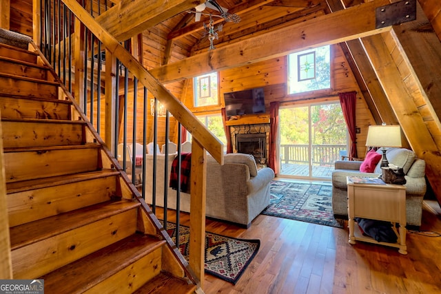 living room with wood walls, wood-type flooring, vaulted ceiling with beams, a fireplace, and wooden ceiling