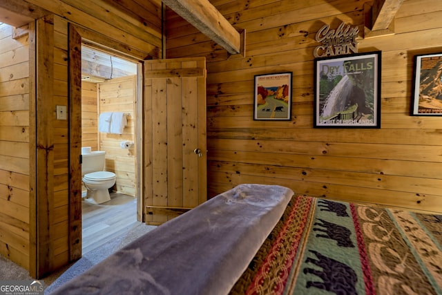 bedroom featuring light hardwood / wood-style floors, wood walls, and ensuite bathroom