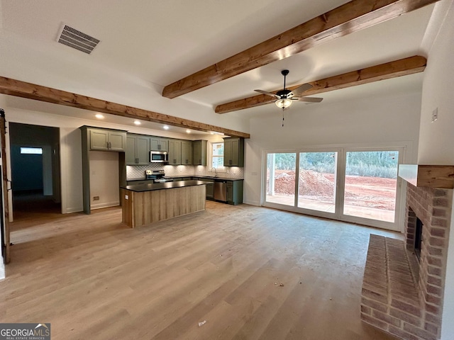 unfurnished living room with beamed ceiling, ceiling fan, a brick fireplace, and light hardwood / wood-style floors