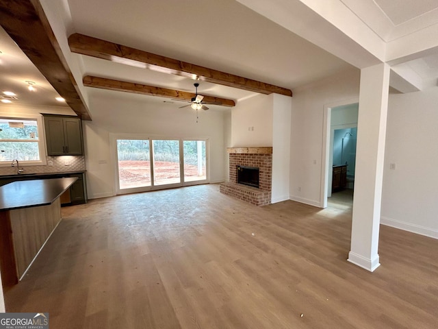 unfurnished living room featuring a brick fireplace, a wealth of natural light, light hardwood / wood-style flooring, and sink