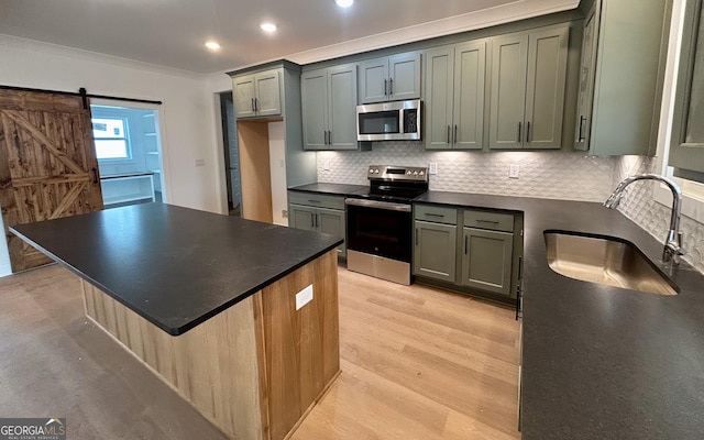 kitchen with appliances with stainless steel finishes, sink, backsplash, light hardwood / wood-style floors, and a barn door