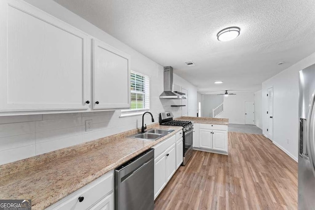 kitchen with wall chimney range hood, white cabinets, light wood-type flooring, sink, and stainless steel appliances