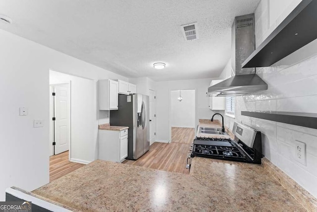 kitchen featuring stainless steel fridge, white cabinets, gas range oven, light hardwood / wood-style floors, and wall chimney exhaust hood