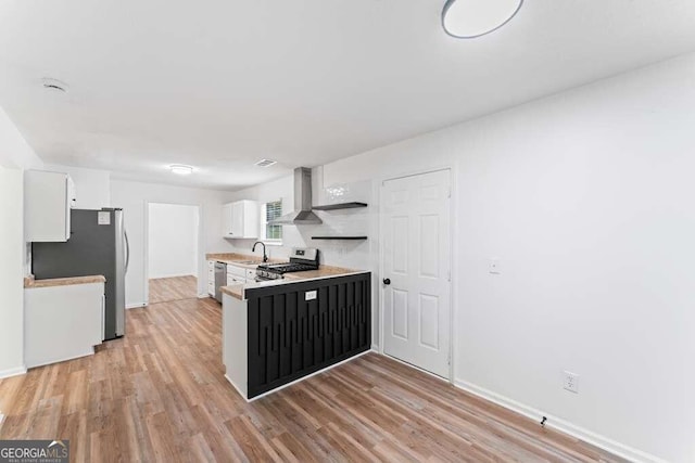 kitchen featuring wall chimney range hood, sink, light wood-type flooring, white cabinetry, and stainless steel appliances