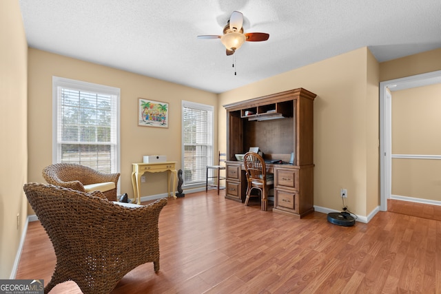 office area with a textured ceiling, light wood-type flooring, and ceiling fan