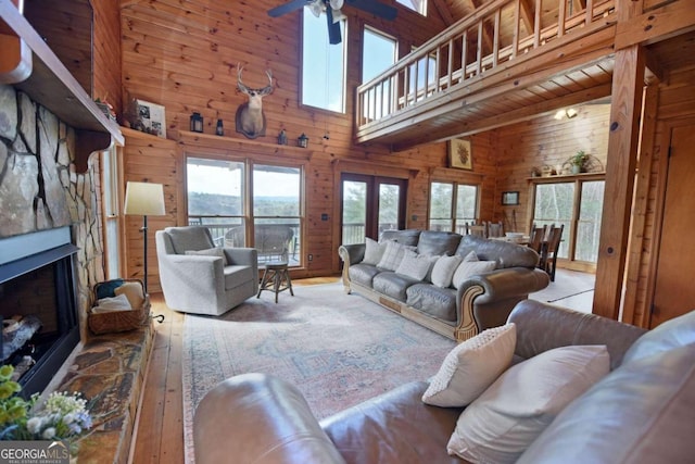 living area with ceiling fan, high vaulted ceiling, wooden walls, a fireplace, and hardwood / wood-style floors