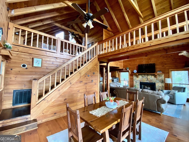 dining area featuring a fireplace, high vaulted ceiling, hardwood / wood-style flooring, ceiling fan, and beam ceiling