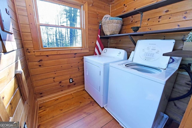 laundry area with light wood-style flooring, laundry area, wooden walls, and washing machine and clothes dryer