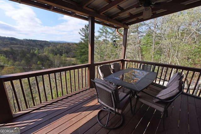 wooden terrace with ceiling fan, outdoor dining space, and a view of trees