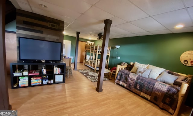 living area featuring a drop ceiling, wood finished floors, visible vents, and a ceiling fan