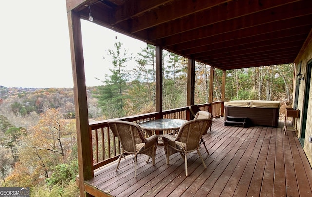 wooden terrace with a hot tub, outdoor dining area, and a wooded view