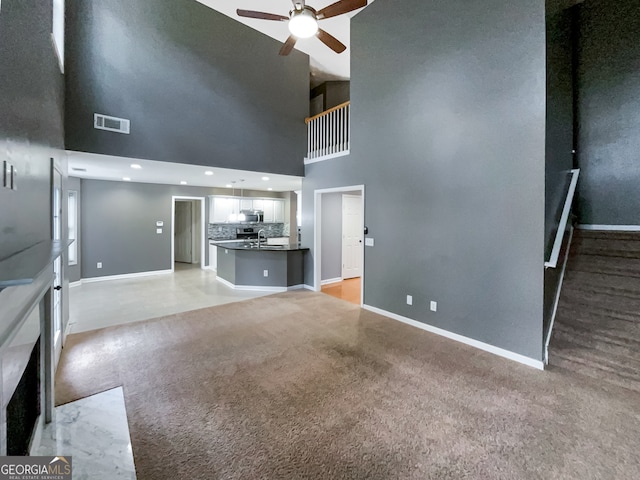 unfurnished living room with ceiling fan, light carpet, a towering ceiling, and sink